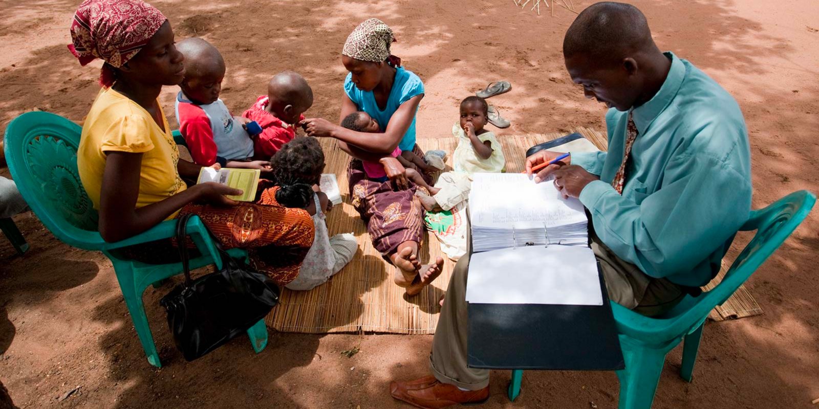 A health worker collects data from two women and their children.